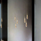 Clérachic Gold-Flecked Glass Teardrop Pendant Lights grouped at staggered heights down a tall concrete stairwell wall, lit.