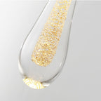 Macro of a Clérachic teardrop pendant drop, coarse gold flakes suspended in a column inside the clear glass.