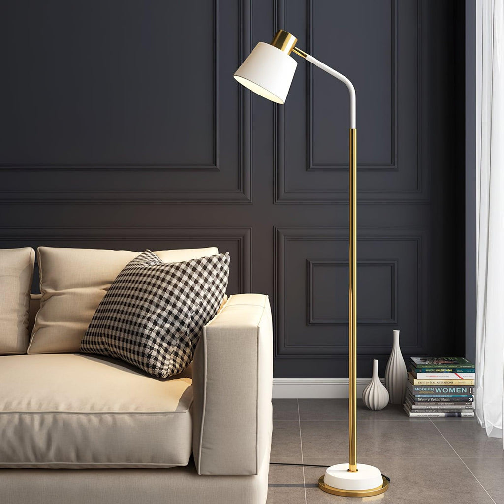 A Clérachic floor lamp with a white shade and gold stem beside a cream leather sofa, against a charcoal panelled wall.