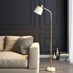 A Clérachic floor lamp with a white shade and gold stem beside a cream leather sofa, against a charcoal panelled wall.