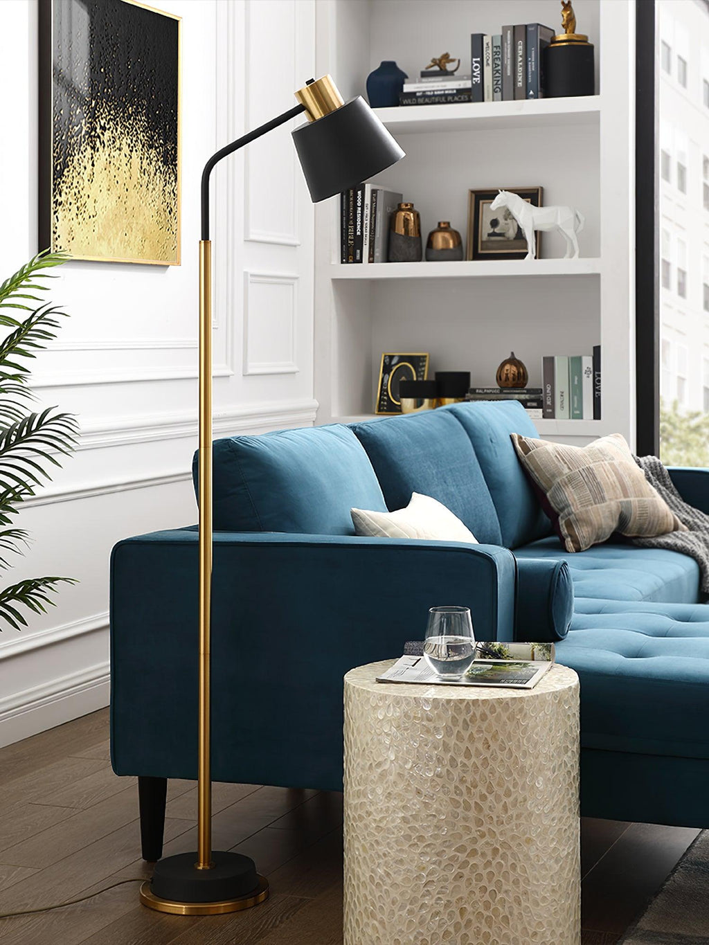 This Clérachic floor lamp, with a black shade and gold stem, stands behind a teal sofa and a mosaic-topped side table.