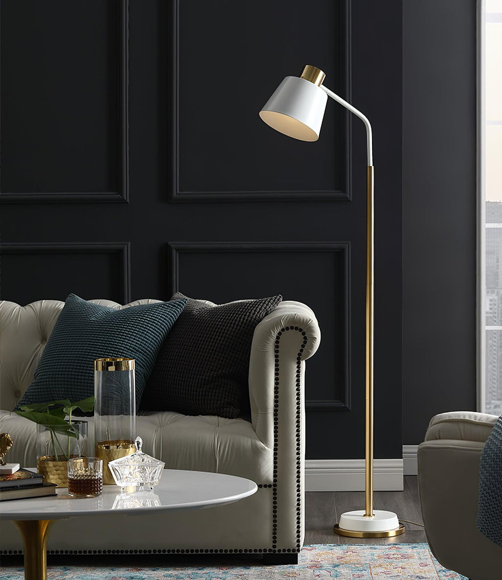 White-shaded Clérachic floor lamp beside a grey buttoned sofa and a round marble coffee table, with a dark panelled wall behind.