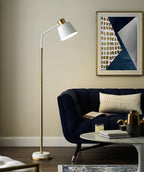 A Clérachic floor lamp with a white shade leans over a navy velvet sofa, beneath a blue and gold abstract print.