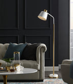 A tall Clérachic floor lamp with a white shade at the end of a grey buttoned sofa, a glass vase and tumblers on the table in front.