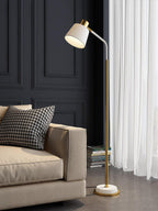 Clérachic floor lamp with a white shade and gold stem in front of a sheer white curtain and a cream sofa arm.