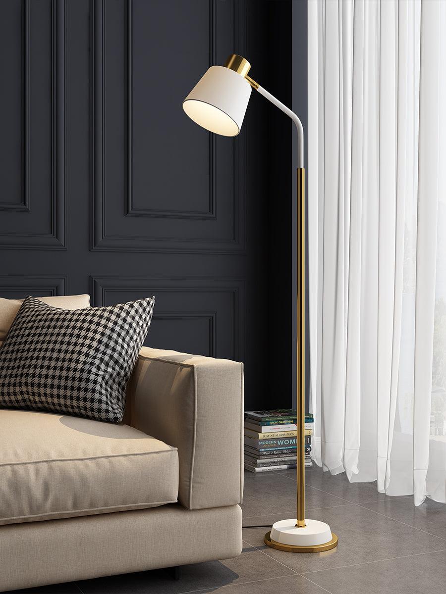 Clérachic floor lamp with a white shade and gold stem in front of a sheer white curtain and a cream sofa arm.