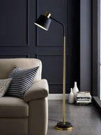 The black-shaded Clérachic floor lamp rises beside a cream armchair, with a stack of books and two white vases at its foot.