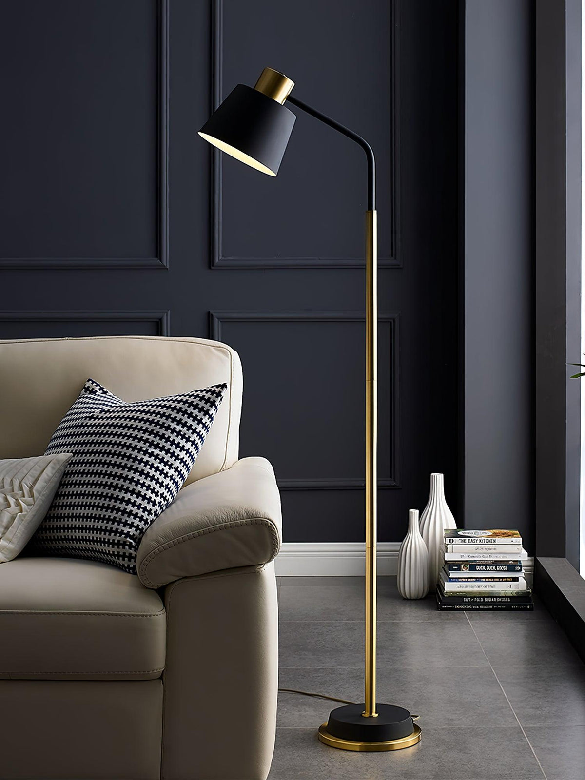 The black-shaded Clérachic floor lamp rises beside a cream armchair, with a stack of books and two white vases at its foot.