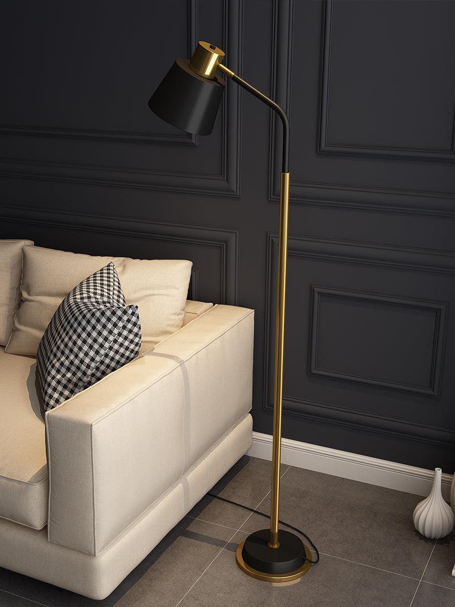 A Clérachic floor lamp with a black shade on a bent arm, beside a cream sofa and a white vase on a grey tiled floor.