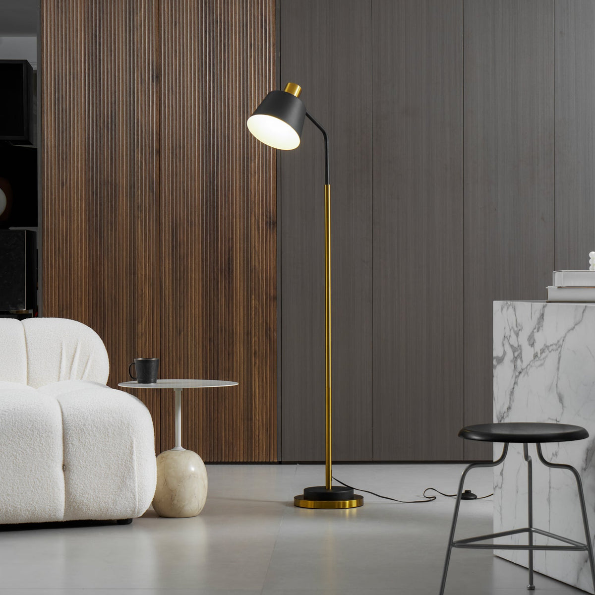 Clérachic floor lamp in black and gold beside a wood-slat wall, a boucle armchair, a round side table and a black stool.