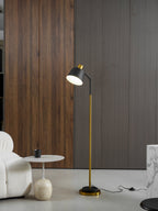 Wider view of this Clérachic floor lamp against a wood-slat wall, with a small round table and a cup on the floor beside it.