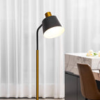 Close view of the black shade, gold collar and curved arm of this Clérachic floor lamp, lit before sheer white curtains.