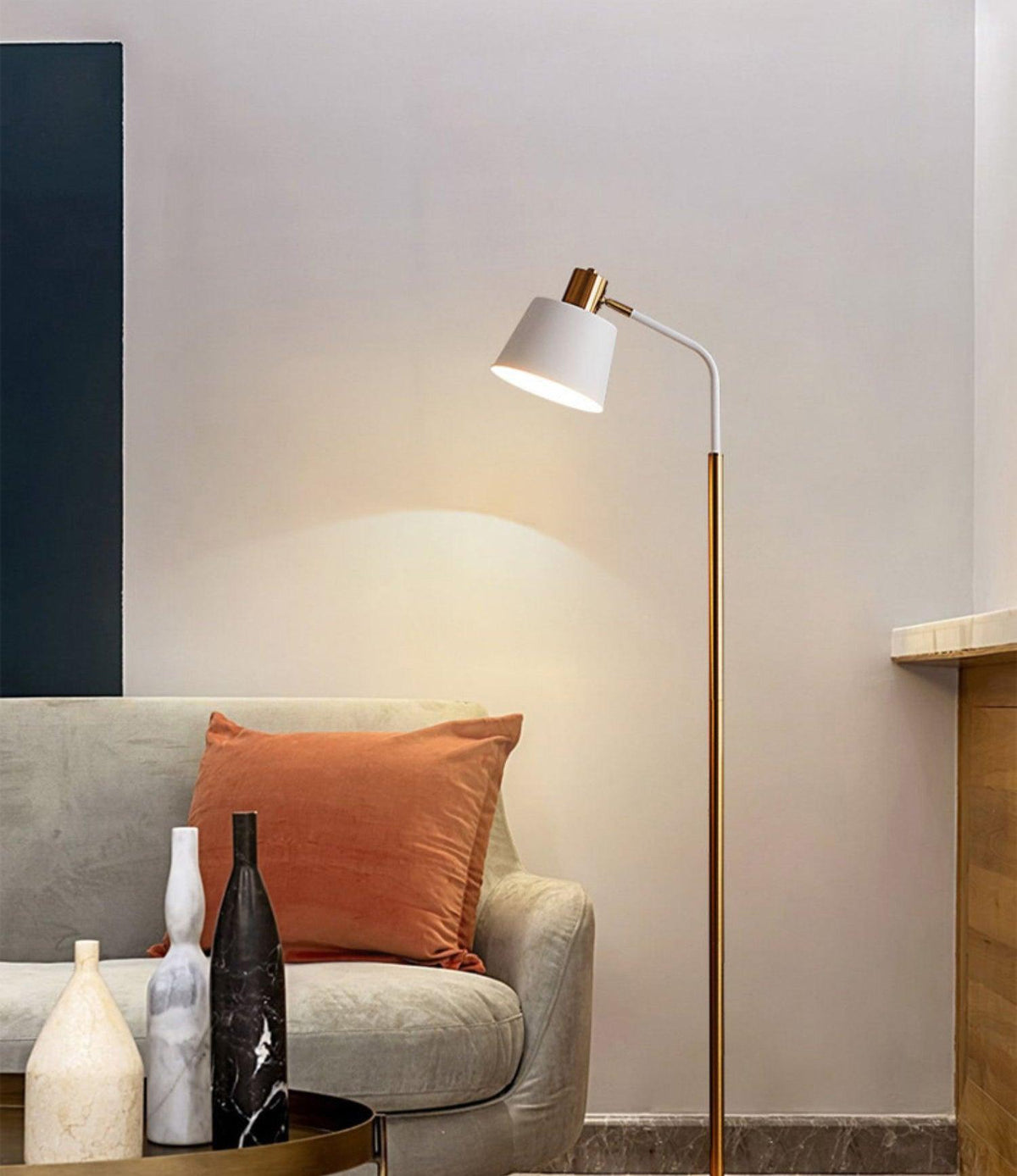 White-shaded Clérachic floor lamp throwing a pool of light on a pale wall, above a grey sofa with a rust-coloured cushion.