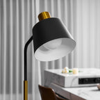 Close view of this Clérachic floor lamp's black shade lit from inside, with grey curtains and a marble table behind.