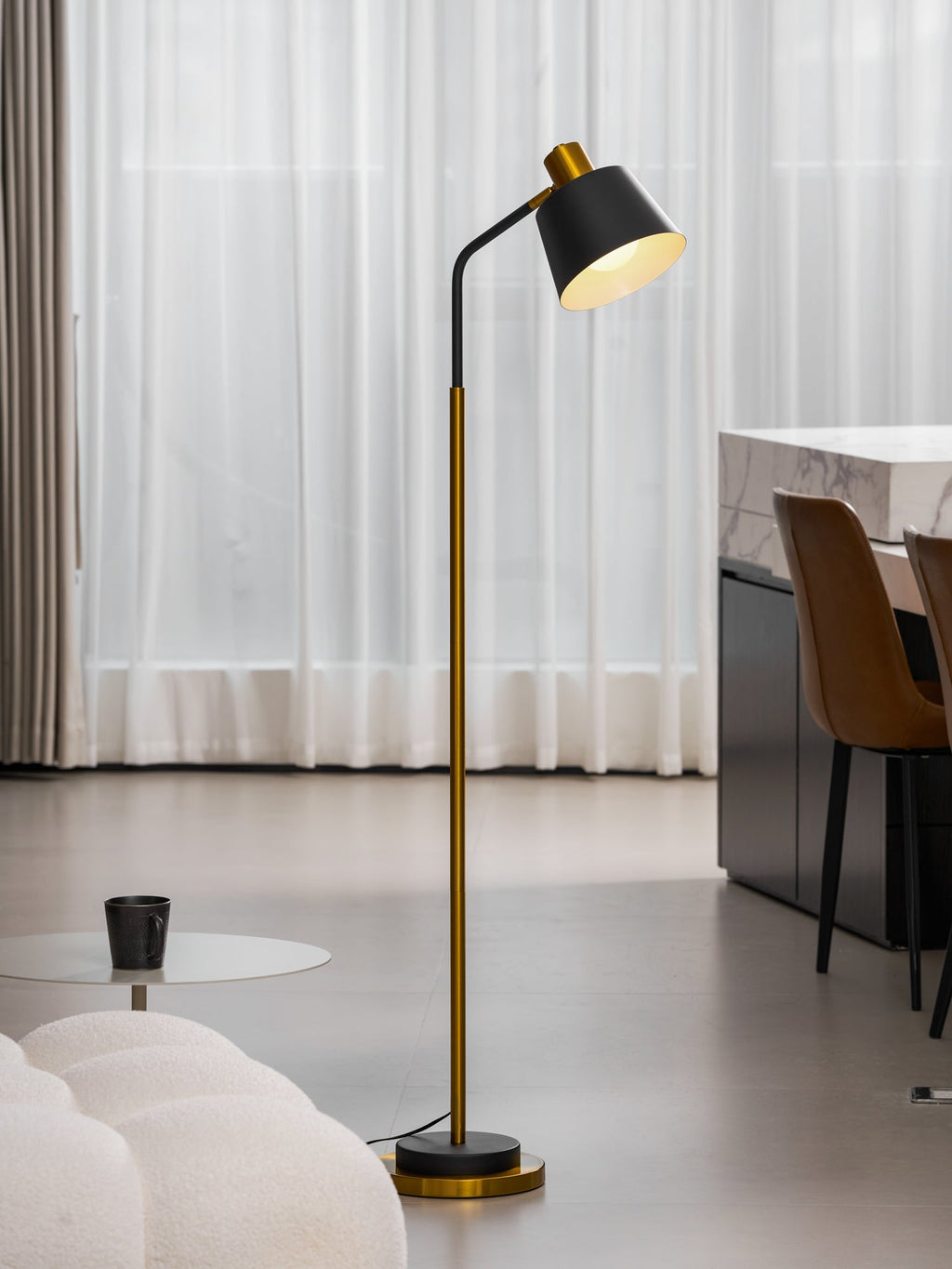 Full-length Clérachic floor lamp in black and gold, lit beside sheer curtains, brown dining chairs and a marble counter.