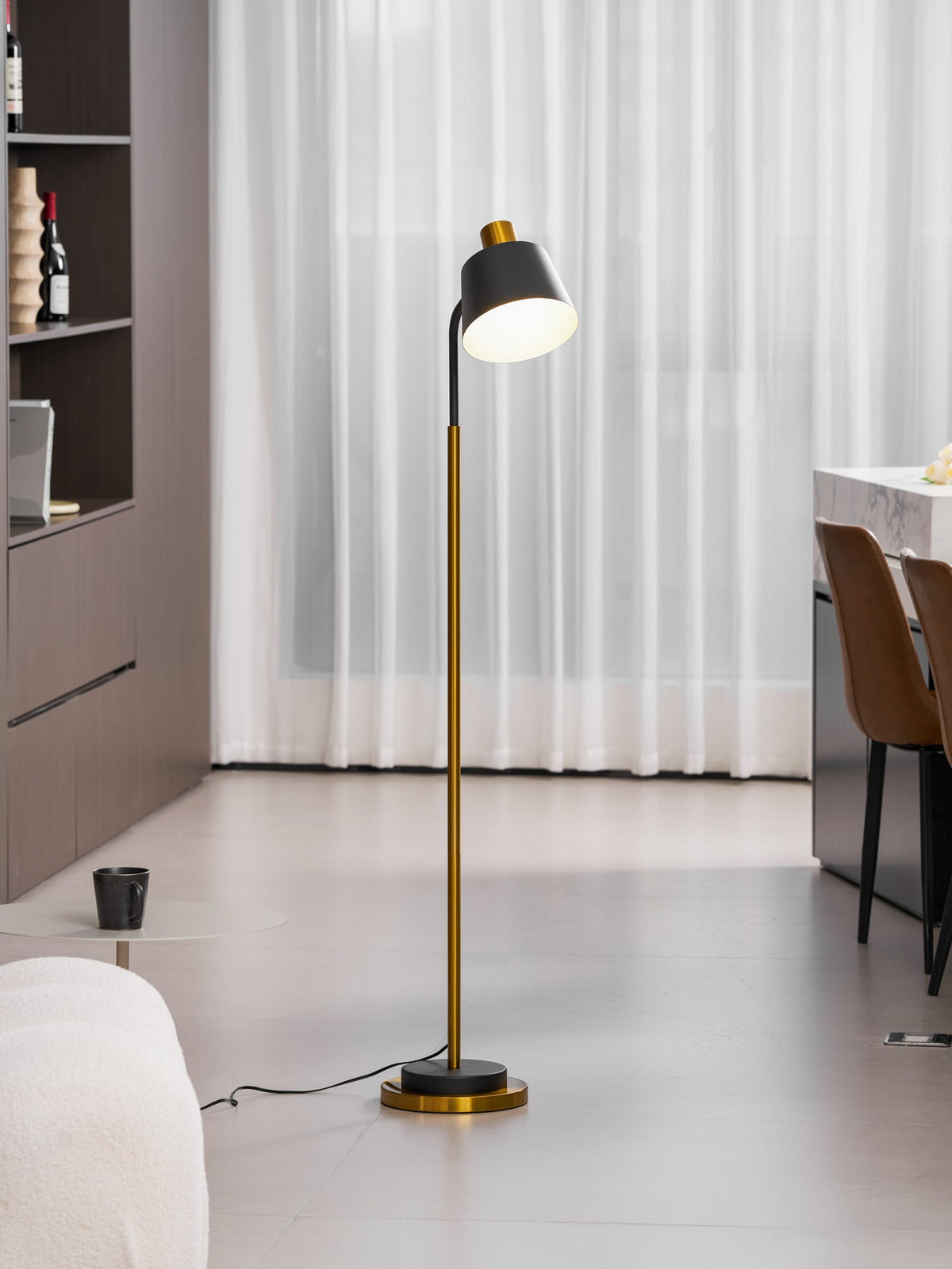 Slim Clérachic floor lamp standing on a pale floor in front of sheer curtains, with a dark shelving unit to its left.