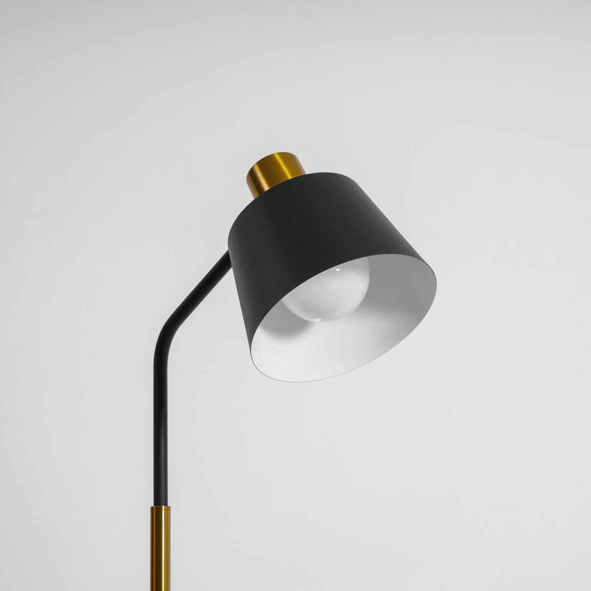 This Clérachic floor lamp's black shade turned further to the side, its white inner surface and bulb visible, on grey.