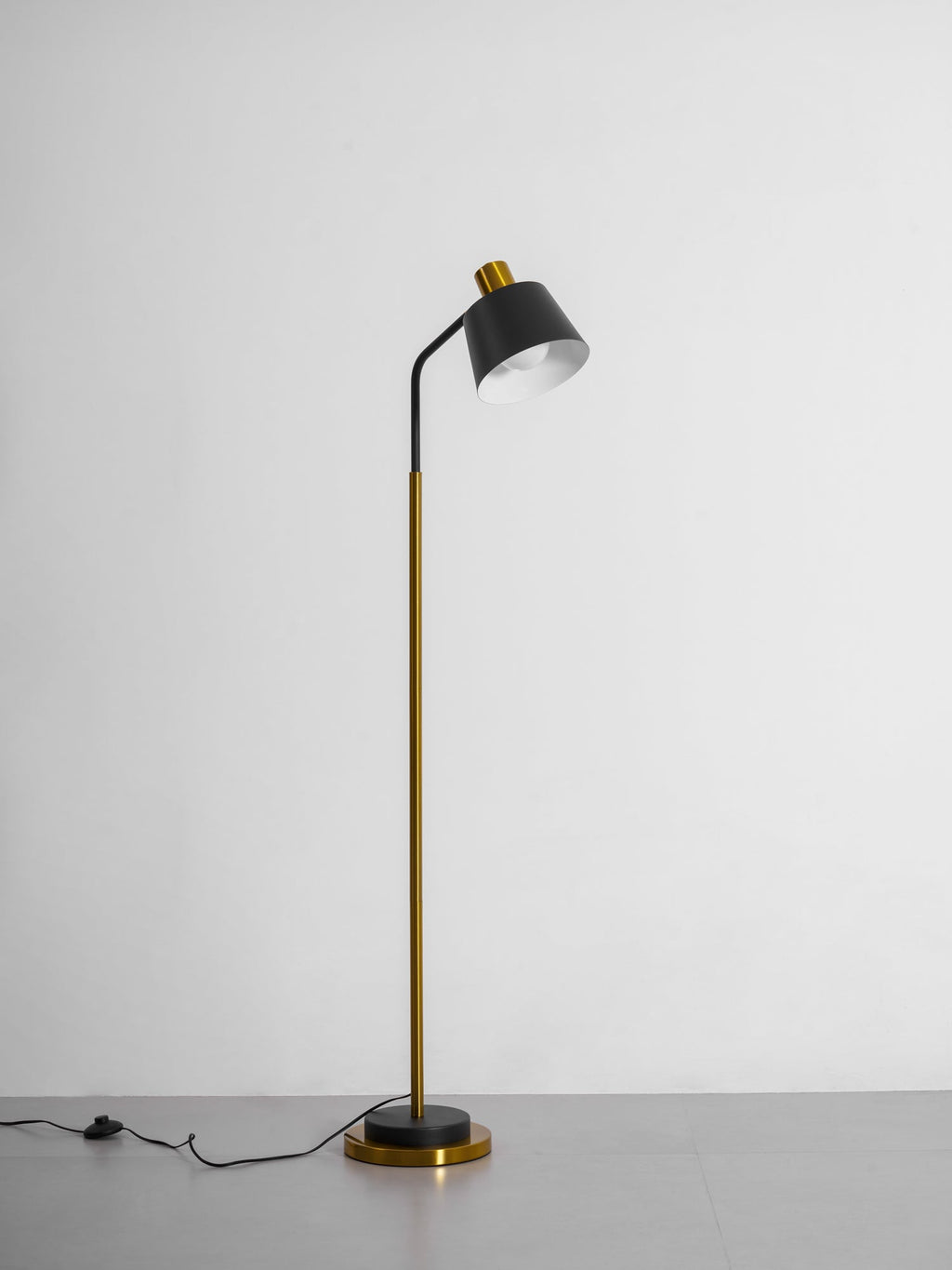 Clérachic floor lamp in black and gold on a grey studio floor, its shade tilted up and the cord switch lying beside the base.