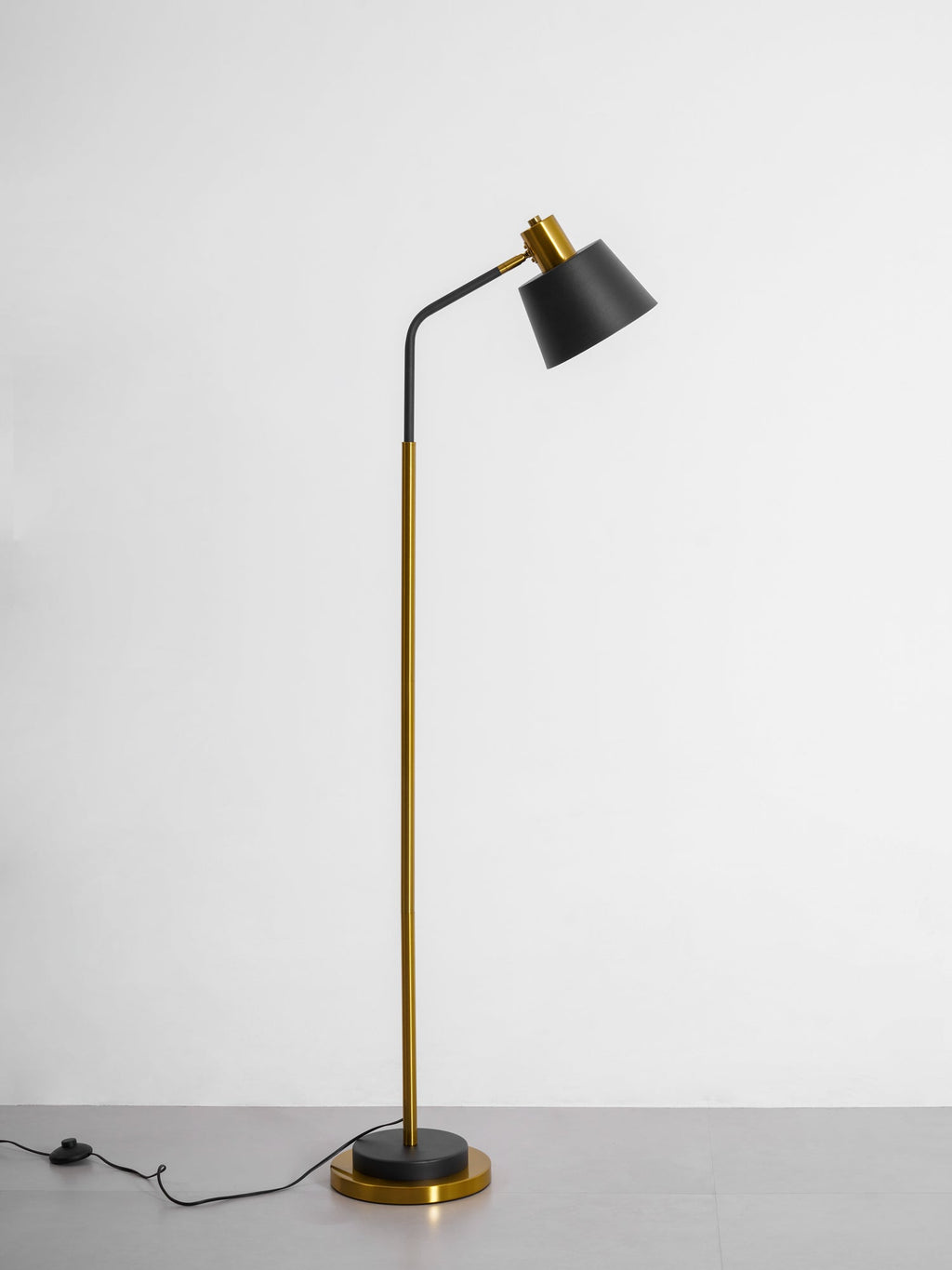 Side view of a Clérachic floor lamp on a grey studio floor, with the shade angled away and its cord running to the left.