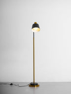 Clérachic floor lamp with its black shade turned upward, the lit inside glowing, on a grey studio floor.