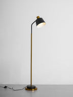 Clérachic floor lamp in black and gold in a grey studio, the shade tilted toward the viewer and the cord on the floor.