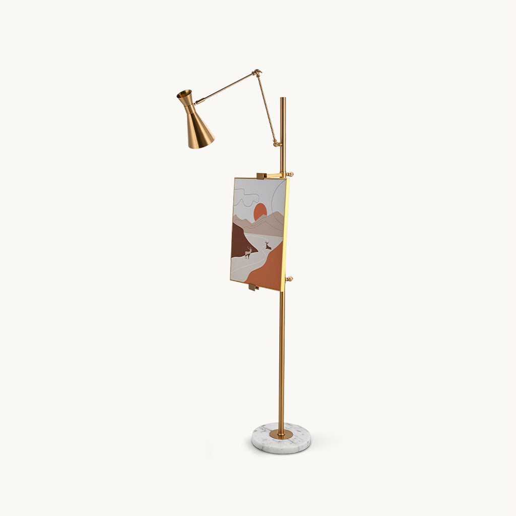 Gold Clérachic floor lamp with a cone shade on an angled arm, a framed picture on its pole and a round white marble base, on a plain backdrop.