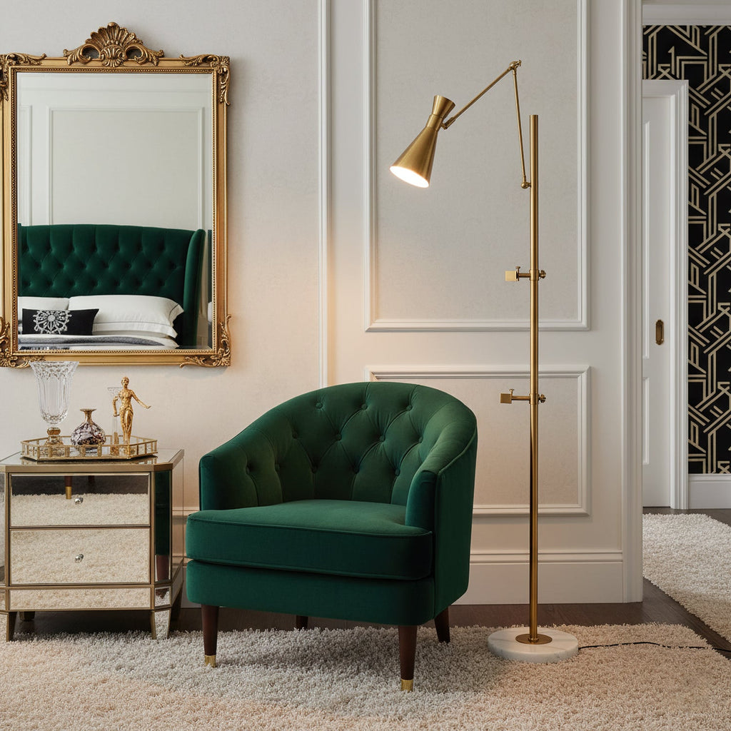 Lit cone shade on a Clérachic gold floor lamp beside a green tufted armchair, with a gold-framed mirror and a mirrored side table.