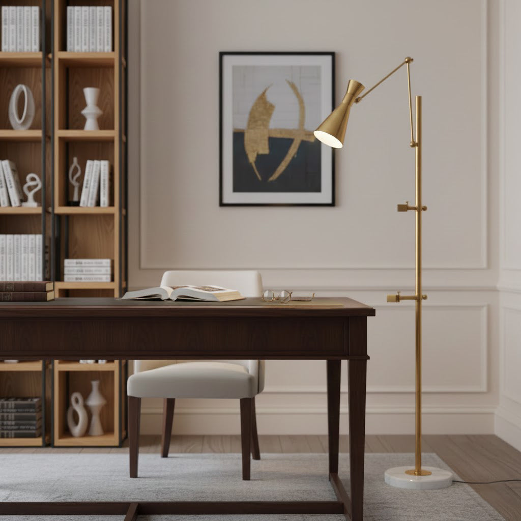 A Clérachic gold floor lamp stands by a dark wood desk with its shade lit toward an abstract print, with open shelves behind.