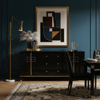 Clérachic floor lamp in gold with a lit cone shade, set against a deep teal wall beside a black sideboard and a large geometric print.