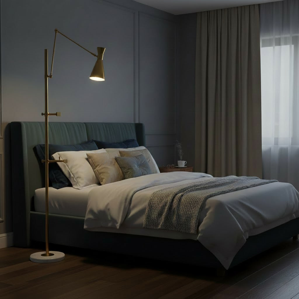 The gold cone shade of this Clérachic floor lamp glows in a dim bedroom, beside a bed with grey and cream bedding and a heavy curtain.