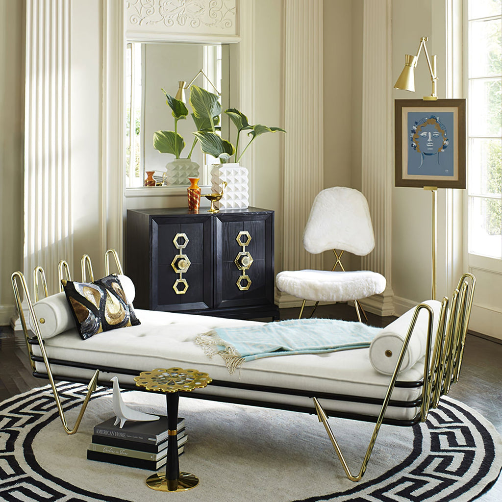 Gold Clérachic floor lamp holding a small framed portrait in an ornate sitting room, behind a white daybed with brass trim and a black cabinet.