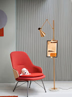 A Clérachic gold floor lamp with a framed copper-toned print, beside a red lounge chair with a small white puppy on the seat.