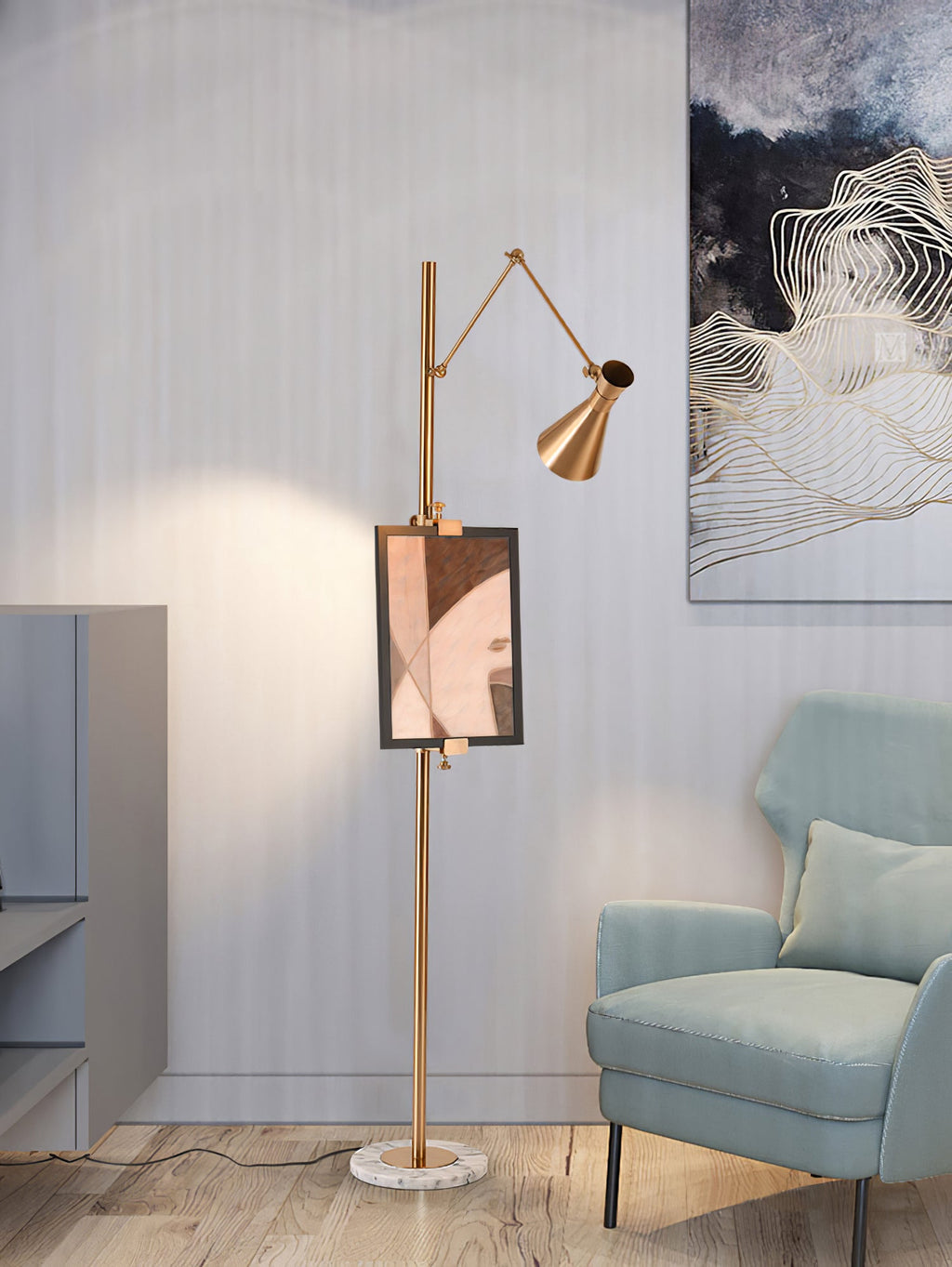 A Clérachic gold floor lamp with a framed print on its pole stands by a pale blue armchair, with a wall-art panel behind.