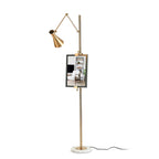 Gold Clérachic floor lamp on a plain white backdrop, with a small framed picture clipped to the pole above a round marble base.