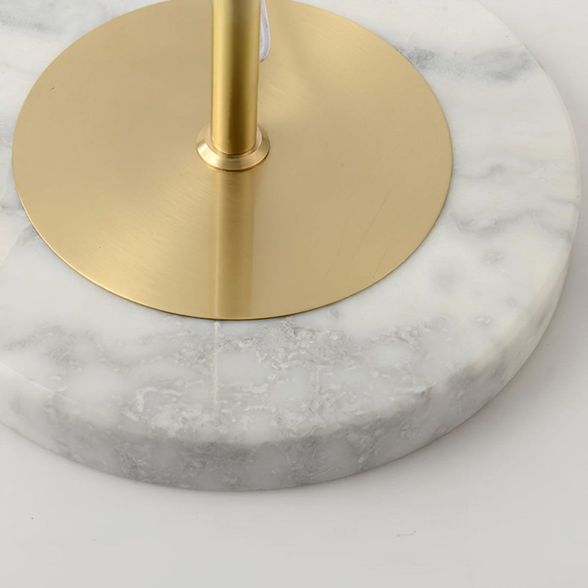 Close view of the round white marble base of this Clérachic floor lamp, with its brushed gold plate and pole at the centre.
