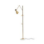 Slim gold Clérachic floor lamp with a cone shade, two clamp arms and a black cord trailing from a marble base, on a white backdrop.
