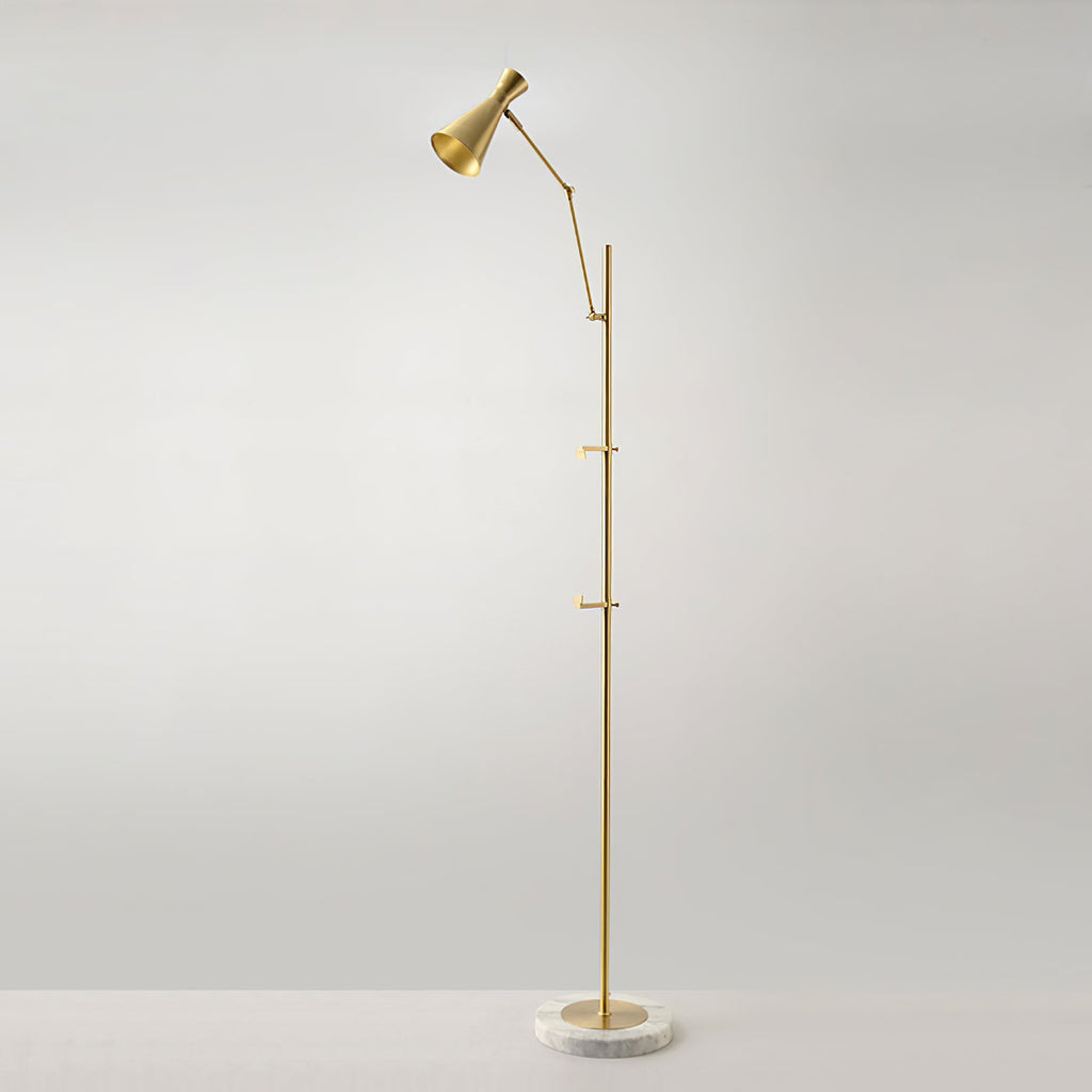 A Clérachic gold floor lamp stands alone against a soft grey wall, with a cone shade at the top and a marble base on the floor.