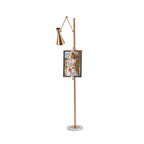 Small view of a Clérachic gold floor lamp with a framed portrait and a cone shade on a long arm, above a marble base on white.
