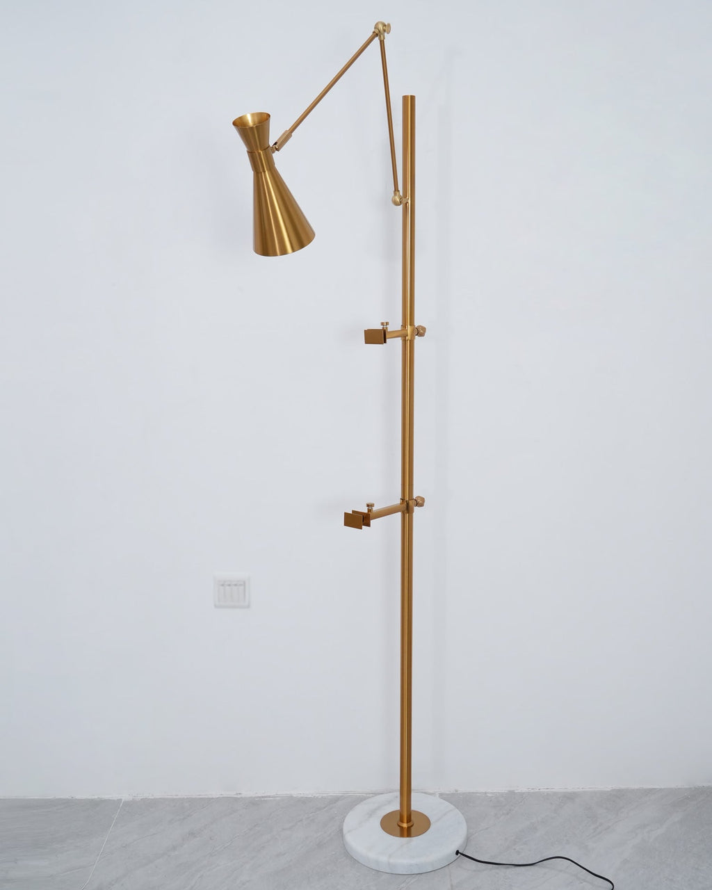 Clérachic gold floor lamp without a picture, showing the two clamp arms on its pole and a cone shade on a white wall.