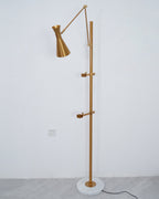 Clérachic gold floor lamp without a picture, showing the two clamp arms on its pole and a cone shade on a white wall.