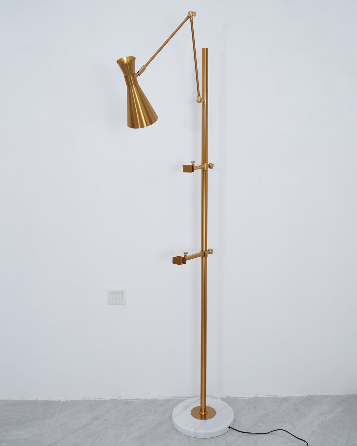 Clérachic gold floor lamp without a picture, showing the two clamp arms on its pole and a cone shade on a white wall.