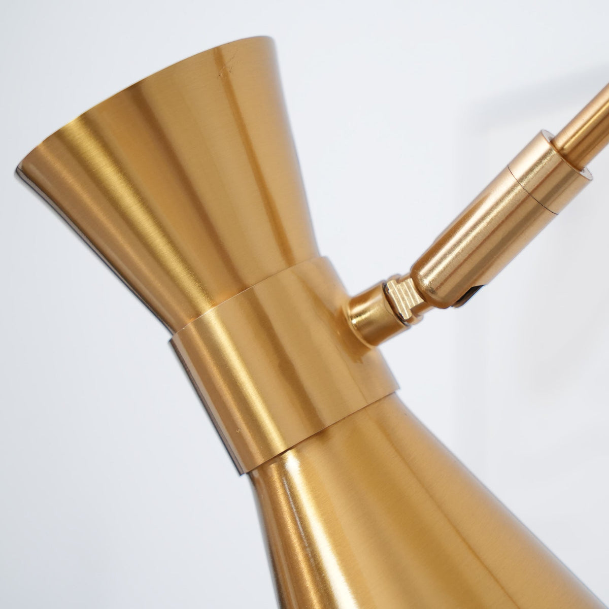 Close view of the hourglass-shaped gold cone shade on this Clérachic floor lamp and its small hinge to the arm.