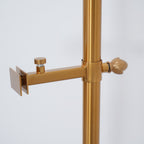Close view of a small clamp arm with a thumb screw on the gold pole of this Clérachic floor lamp, capped by a decorative finial.
