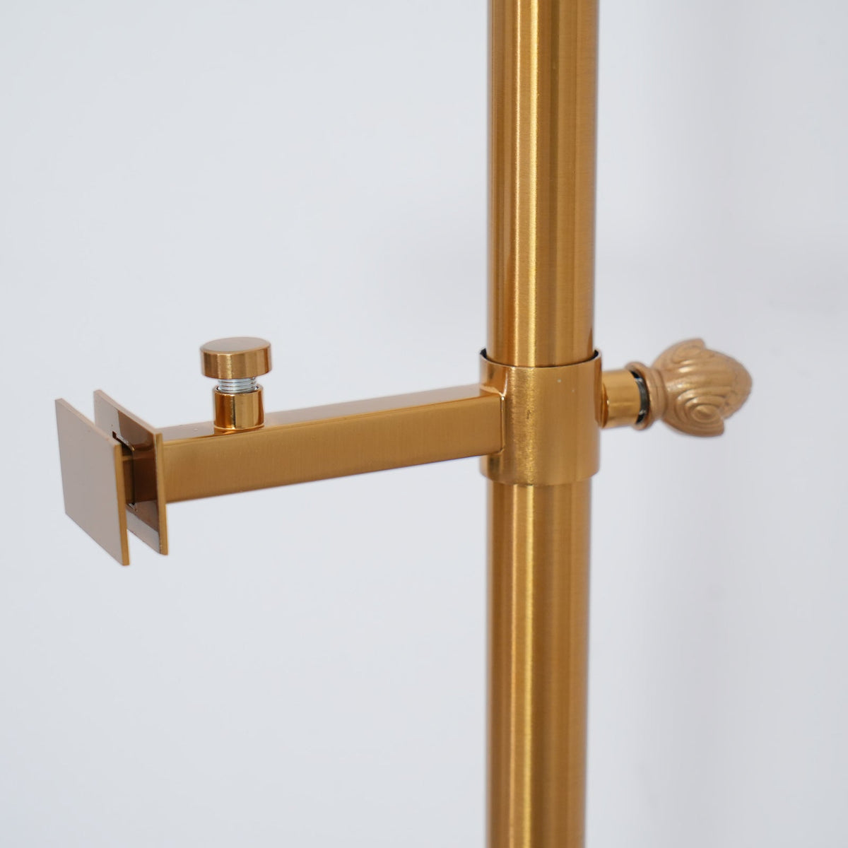 Close view of a small clamp arm with a thumb screw on the gold pole of this Clérachic floor lamp, capped by a decorative finial.