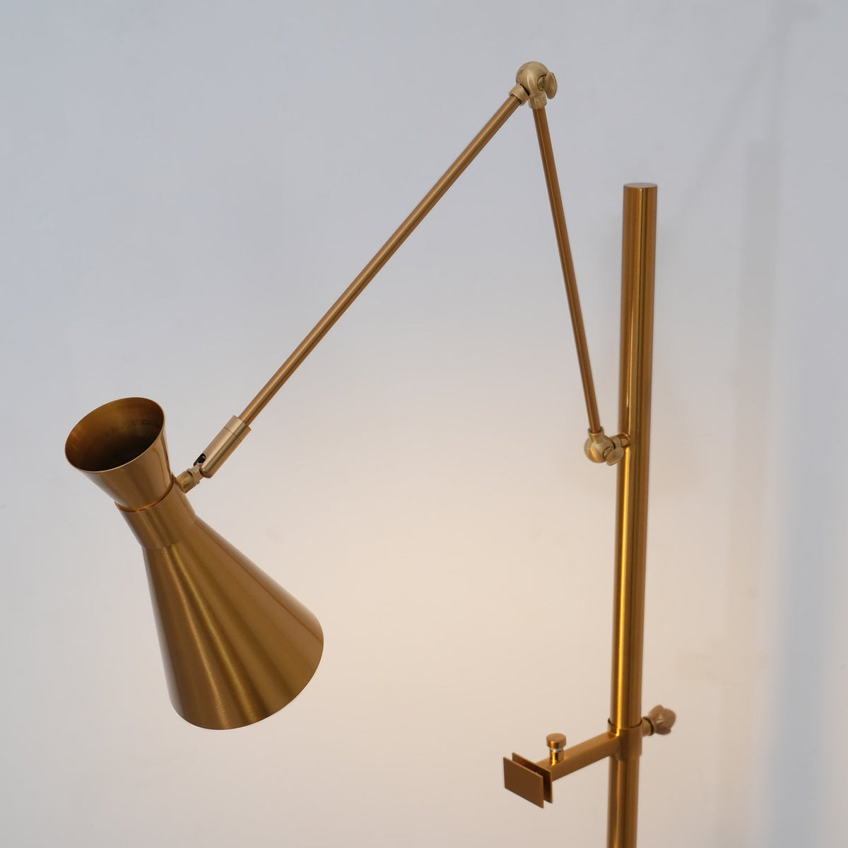 Close view of the long angled arm, brass joint and cone shade of this Clérachic floor lamp, with a clamp arm lower on the pole.