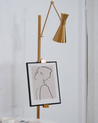 Gold cone shade and a framed line drawing on the pole of a Clérachic floor lamp, seen from a lower angle in a white room.