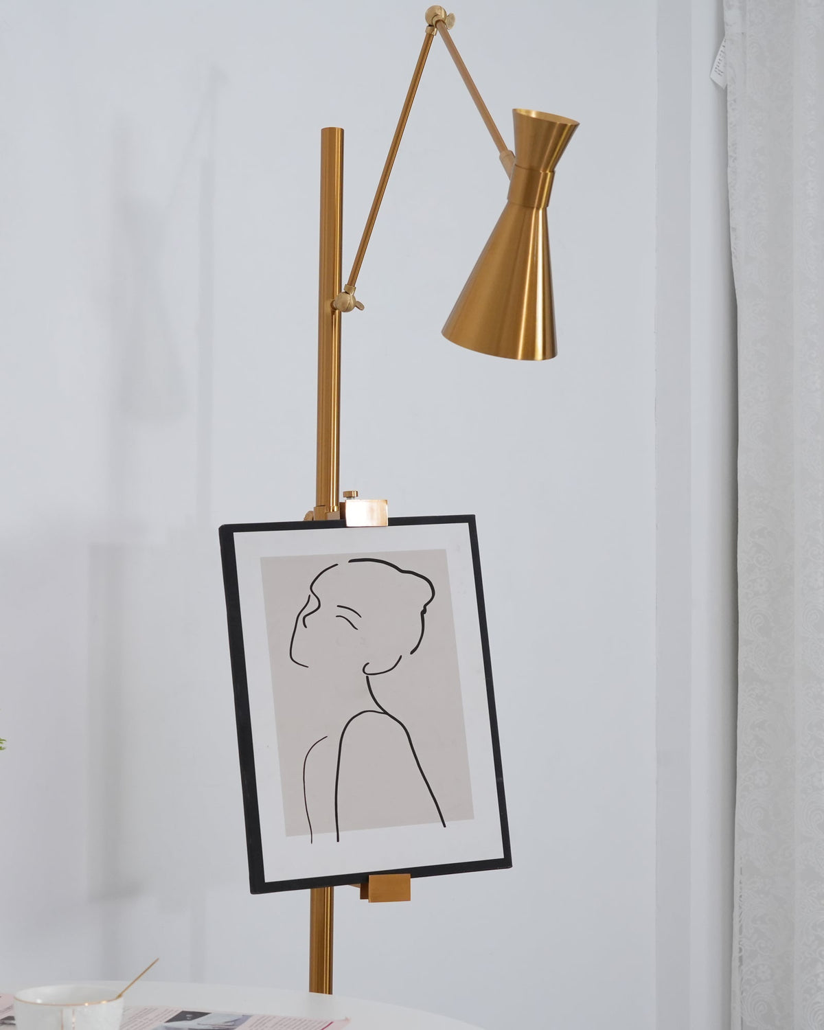 Gold cone shade and a framed line drawing on the pole of a Clérachic floor lamp, seen from a lower angle in a white room.