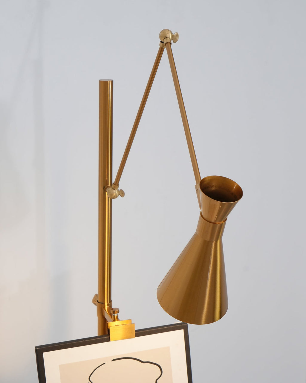 Close view of the arm folded high on the pole of a Clérachic gold floor lamp, with a framed drawing at the bottom of the frame.