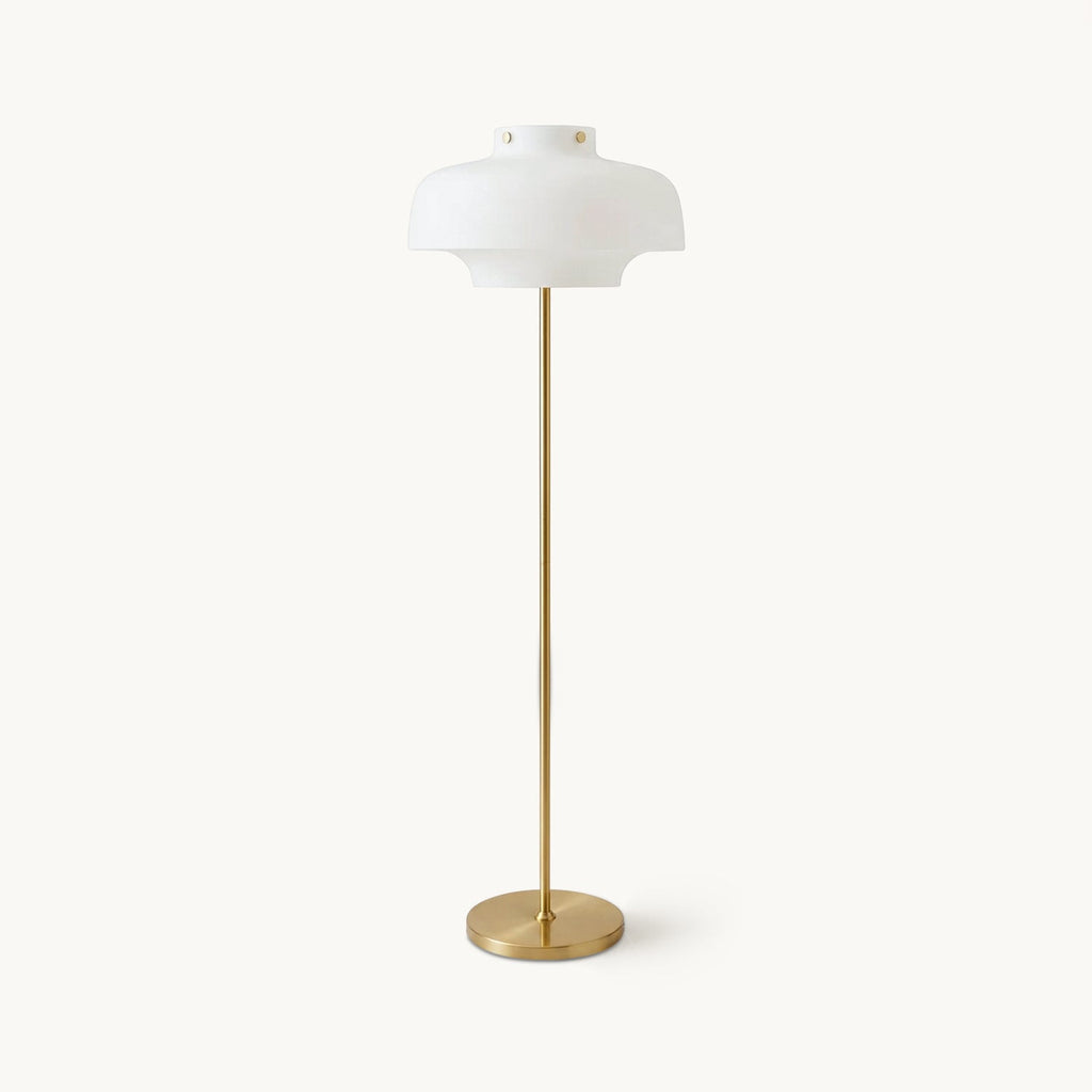 A Clérachic floor lamp with a domed white glass shade on a slim brass stem and round brass base, on a plain off-white backdrop.