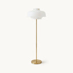 A Clérachic floor lamp with a domed white glass shade on a slim brass stem and round brass base, on a plain off-white backdrop.